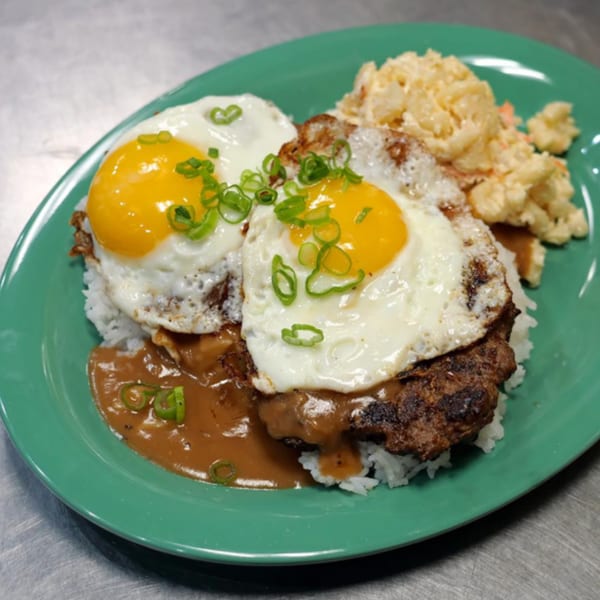 Loco Moco with two fried eggs, gravy, rice, and macaroni salad on a green plate.