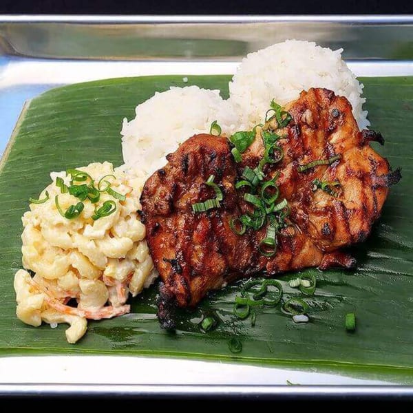 Grilled chicken adobo with rice and macaroni salad, garnished with green onions on a banana leaf.