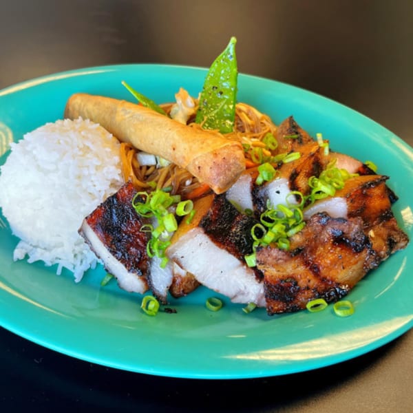 Filipino dish with grilled pork belly, white rice, pancit noodles, lumpia, and green onions on a teal plate.