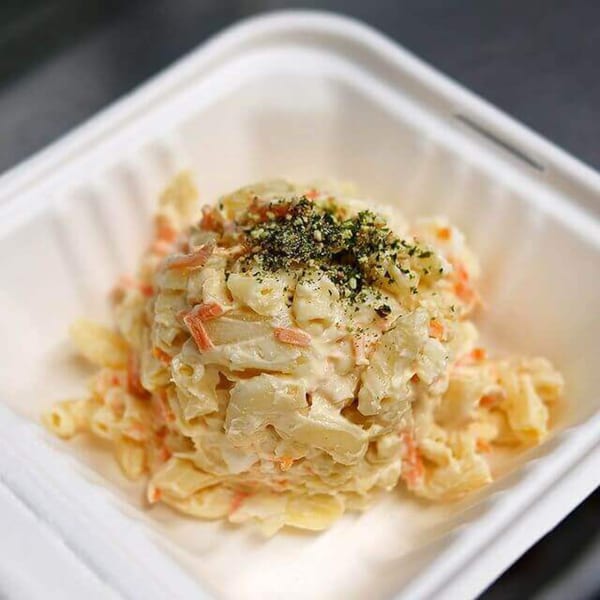 A close-up of creamy macaroni salad with shredded carrots and green seasoning in a white container.