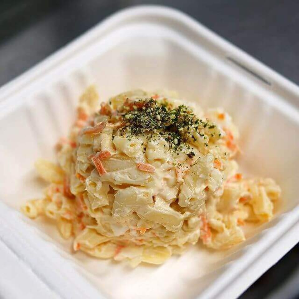 A close-up of creamy macaroni salad with shredded carrots and green seasoning in a white container.