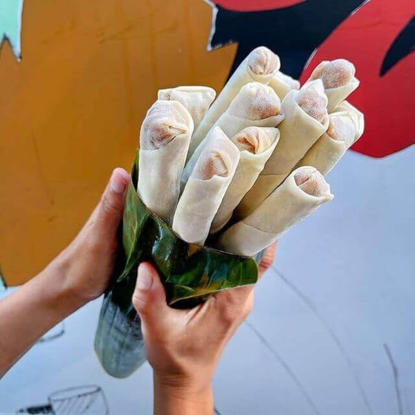 Hands holding a bouquet of uncooked Filipino lumpia wrapped in a banana leaf.