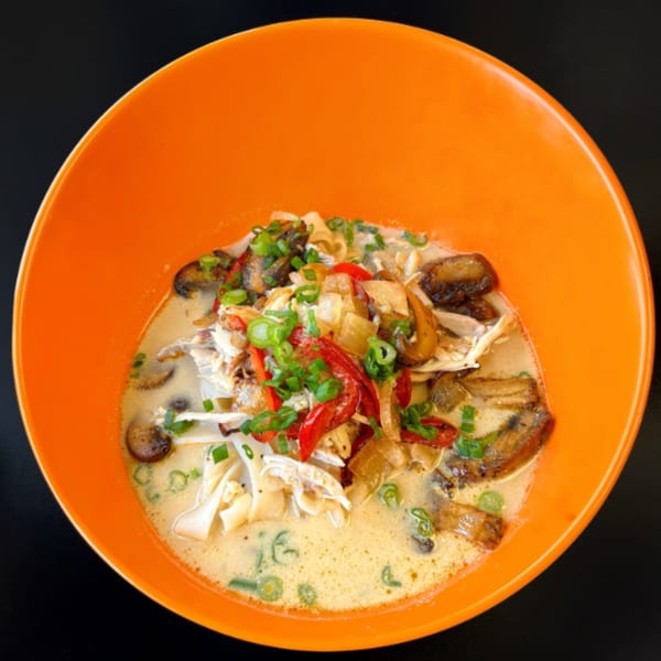 Filipino chicken soup with mushrooms, red peppers, and green onions in an orange bowl.