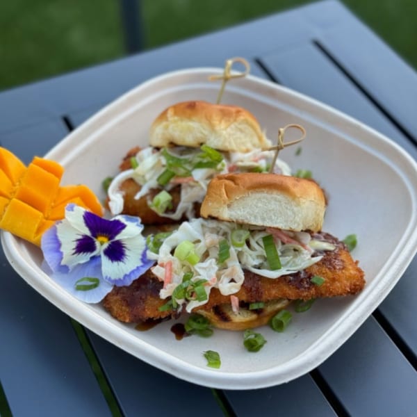 Two Filipino chicken sliders with slaw, green onions, mango, and a flower on a white plate.